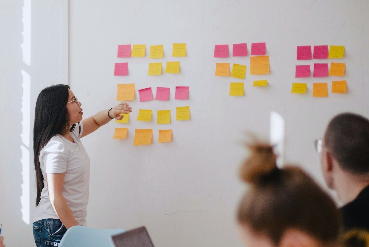 Person zeigt in einem Workshop auf verschiedenfarbige Notizzettel