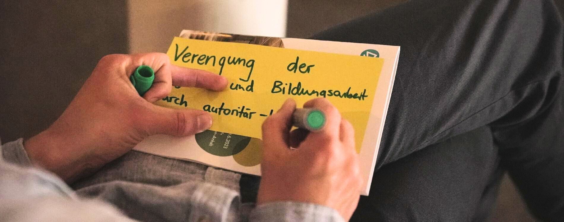 Person schreibt Statement zu Bildungsarbeit auf eine Moderationskarte